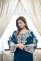 Woman wearing a blue embroidered dress in a decorated room with white curtains.