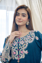 Woman wearing a blue embroidered top with a blurred white curtain background