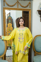 A woman models a bright yellow traditional three-piece salwar kameez suit with floral embroidery on the neckline and hem, standing in front of an ornate gold-framed mirror in an elegant room.