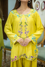 Person wearing a yellow embroidered outfit sitting on a chair.