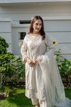 Woman in a white traditional outfit standing outdoors with greenery in the background