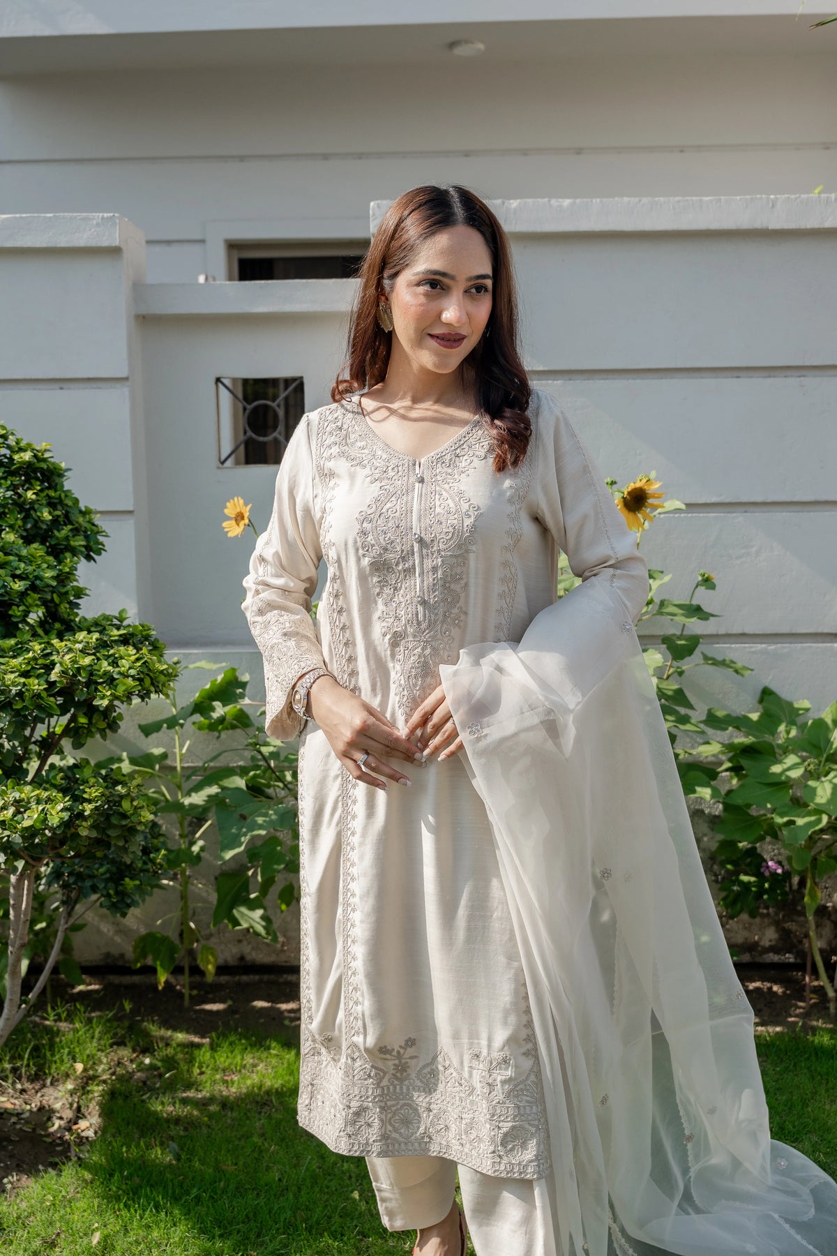 Woman in a white traditional outfit standing outdoors with greenery in the background