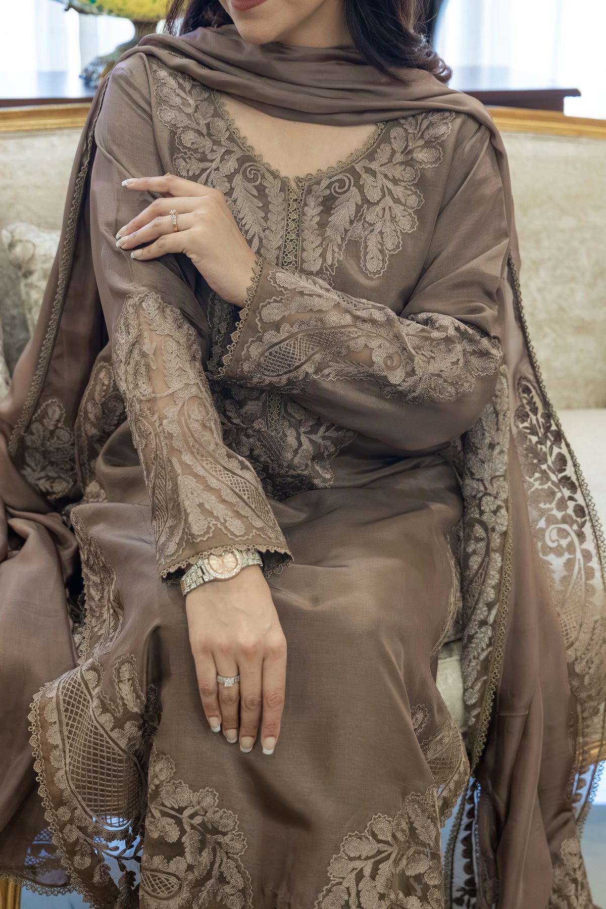 Woman wearing a brown embroidered outfit with a matching shawl indoors.